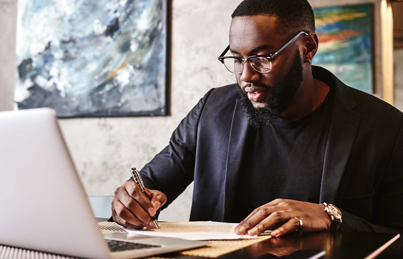 man looking at his laptop while writing on paper-managing his finances