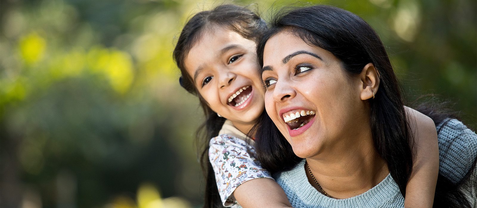 mom and daughter laughing together while daughter rides piggy back on mom