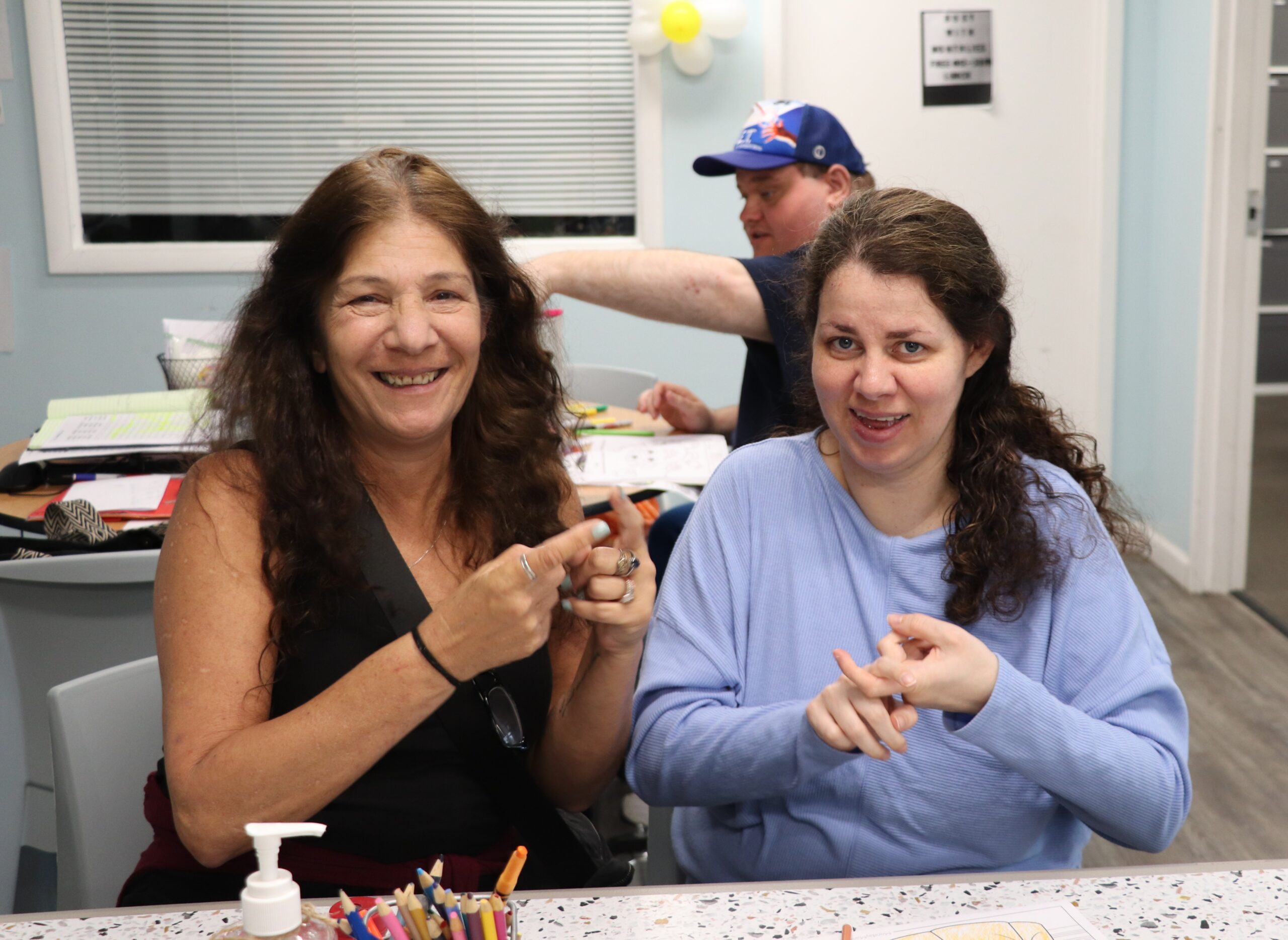 Two women smiling signing the word friend in American Sign Language ASL.